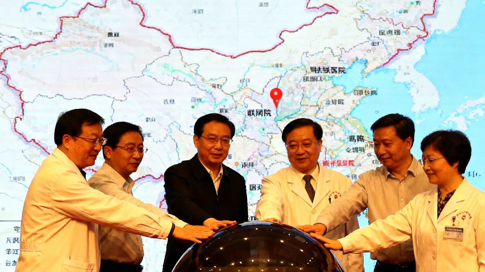 中国中西部地区县域医院远程会诊网络启动仪式的现场照片，多位医疗界人士共同按下启动按钮，背景大屏幕显示联网医院分布地图。